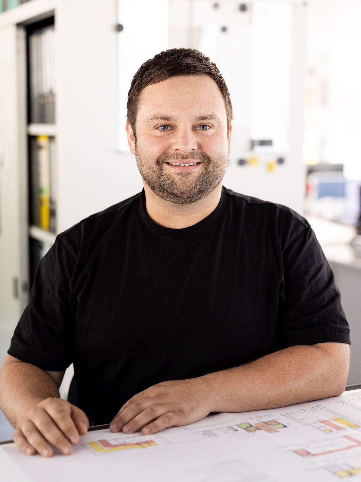 Mann mit Bart sitzt entspannt am Tisch und schaut lächelnd in die Kamera