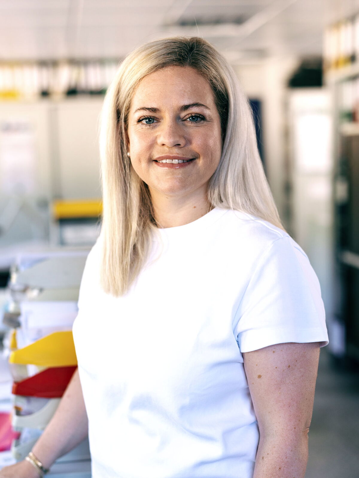 Frau im weißen Oberteil steht im modernen Büro und lächelt freundlich