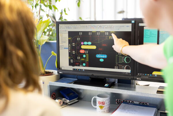 Zwei Personen betrachten eine digitale Anlagenübersicht auf einem Monitor.