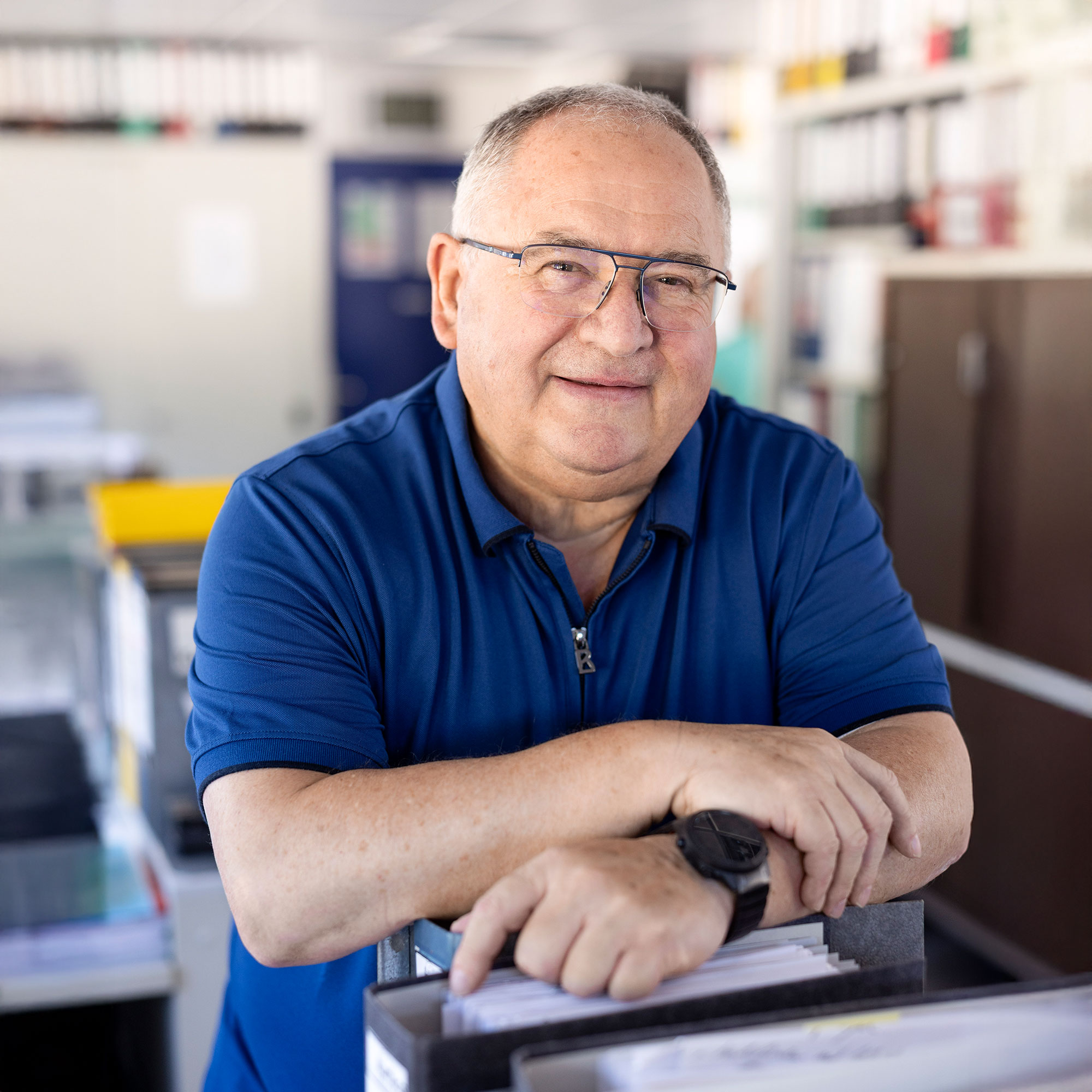 Mann mit Brille sitzt entspannt an einem Tisch und blickt freundlich in die Kamera