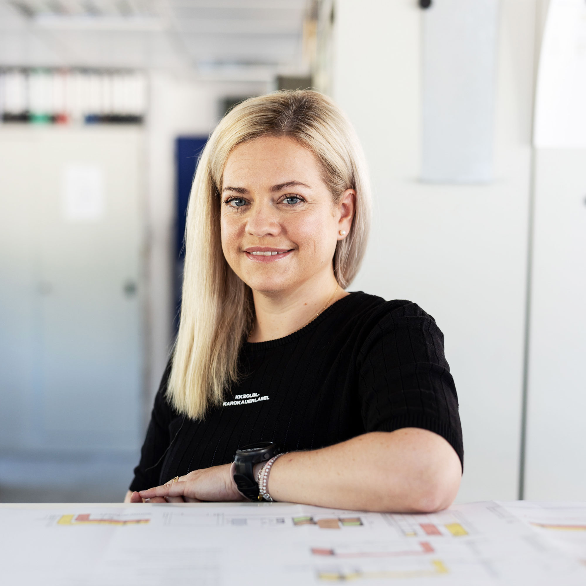 Eine Frau in dunkler Kleidung steht am Schreibtisch in einem Büro
