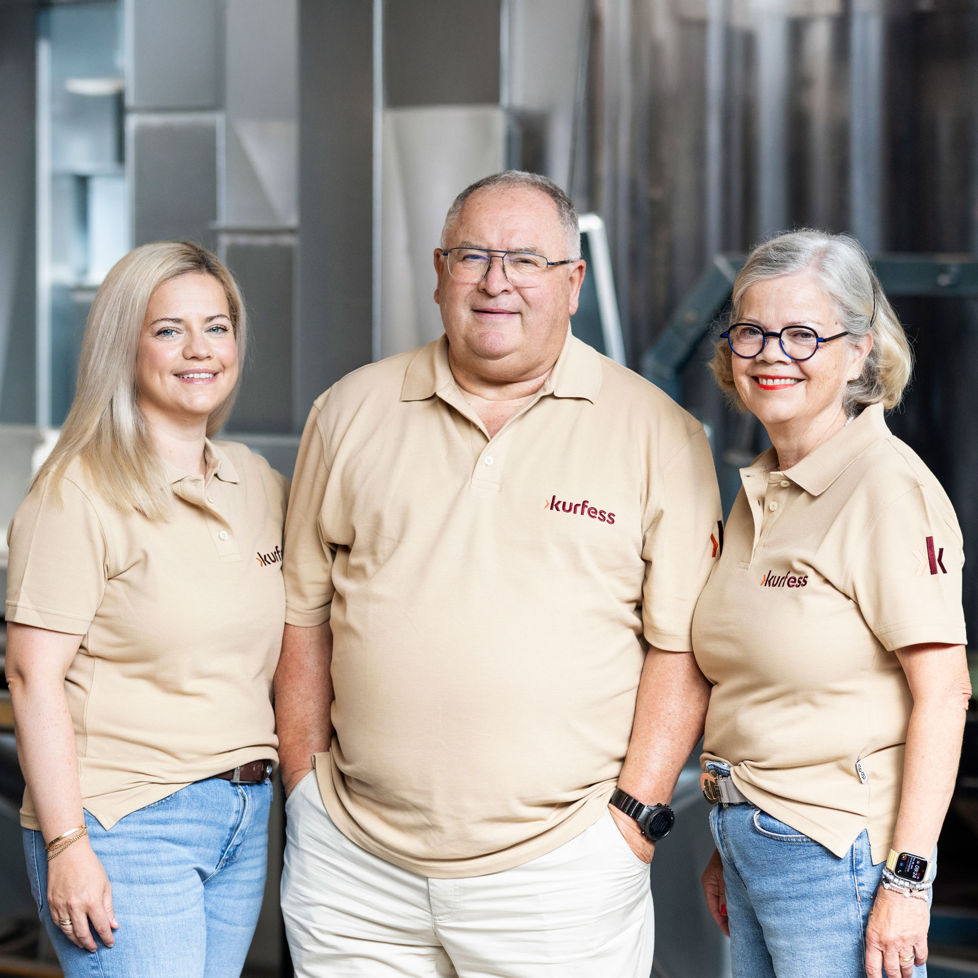 Drei Mitarbeitende stehen gemeinsam im Arbeitsoutfit vor der Kamera und wirken nahbar