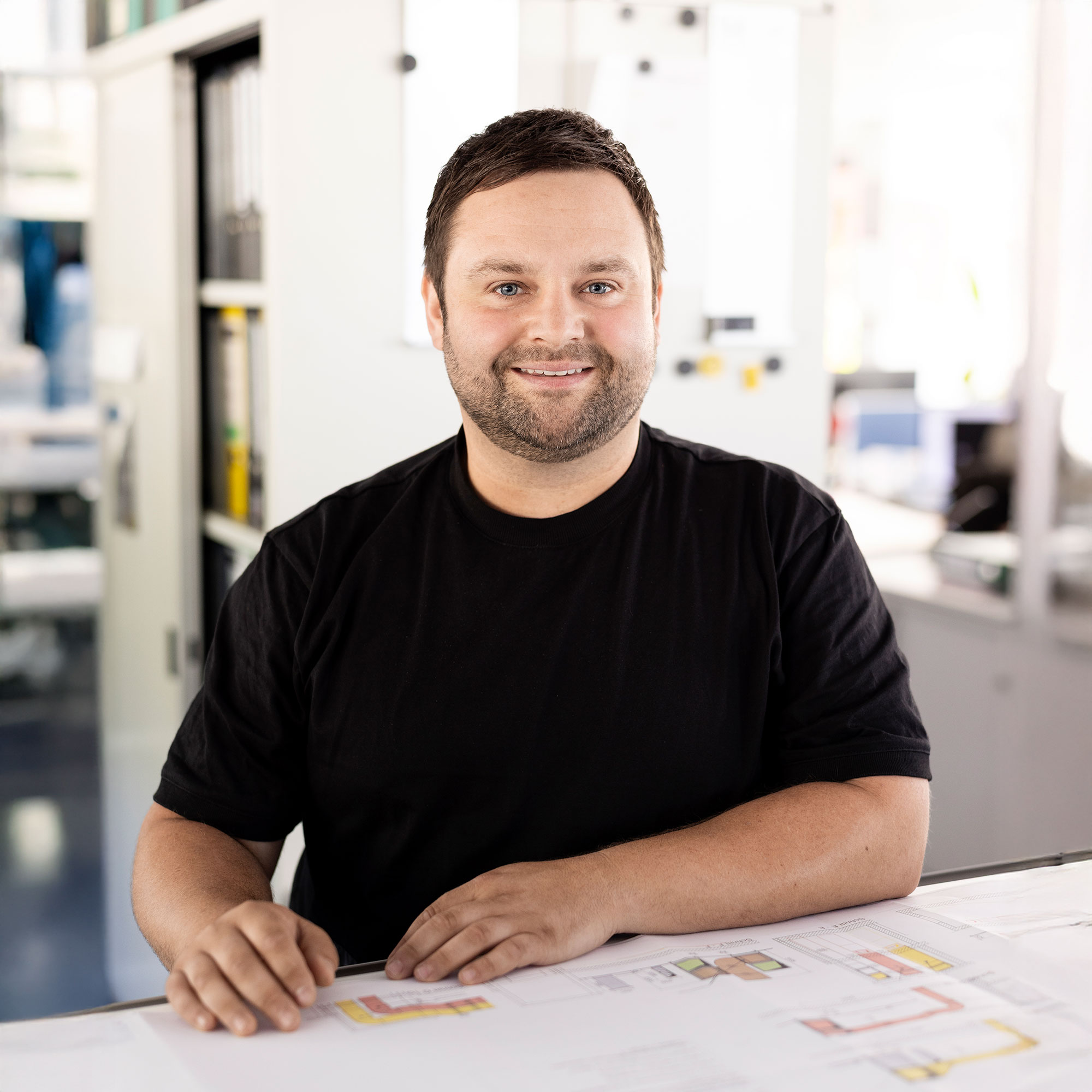 Mann mit Bart sitzt entspannt am Tisch und schaut lächelnd in die Kamera